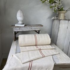 towels are folded on a bench in front of a vase with white flowers and an old wooden table