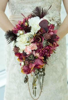 a woman in a wedding dress holding a bouquet with flowers and feathers on her arm