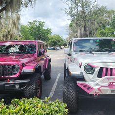 two pink jeeps parked next to each other in a parking lot with trees behind them