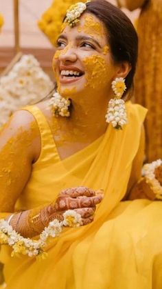 a woman with yellow paint on her face and flowers in her hair, sitting down