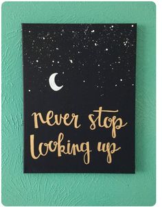 a black and gold sign that says never stop looking up with the moon in the background