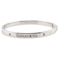 A Tiffany & Co. Diamond bangle, made of 18ct White Gold, and weighing 38.7 gm. Stamped: Tiffany & Co. AU 750. The bangle is set with 2 round, brilliant cut Diamonds, colour D-E and clarity VVS with a total weight of 0.10 ct. Metal: 18ct White Gold Carat: 0.10ct Colour: D-E Clarity: VVS Cut: Round Brilliant Weight: 38.7 grams Engravings/Markings: Signed Tiffany & Co. AU 750. Size/Measurement: Size Medium Current Condition: Excellent - Consistent with age and use. Accompanied by: This Tiffany & Co Tiffany And Co Diamond, Tiffany And Co Bracelet, Tiffany And Co, Diamond Bangle, Hinged Bangle, Brilliant Cut Diamond, Round Brilliant Cut, Tiffany & Co., Round Brilliant