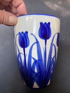 a hand holding a blue and white cup with flowers painted on the outside of it