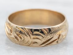 a gold wedding ring with an intricate design on the outside and inside, sitting on a white surface