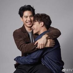 two young men hugging each other while sitting on a stool in front of a gray background