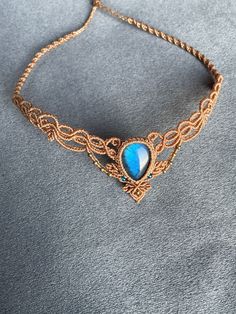 a gold chain necklace with a blue stone on the front and side, sitting on a gray surface