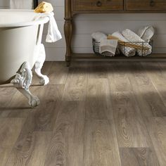 a bathroom with wood flooring and white bathtub next to a wooden dresser in the corner