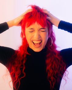 a woman with red hair is laughing and holding her hands on her head while wearing black