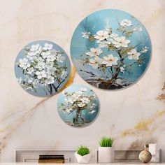 three round paintings with white flowers on a blue background are hanging above a fireplace mantel