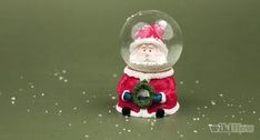 a snow globe with a santa clause holding a wreath in it's lap and standing on the ground