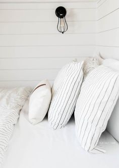 a bed with three pillows and two lights on the headboard, in front of a white painted wall