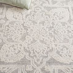 a white and grey rug with an intricate design on the bottom, next to a pillow