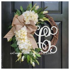 a wreath with white flowers and a monogrammed letter is hanging on the front door