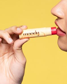 a woman holding a lip bale to her mouth with the word boody written on it