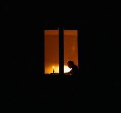 a person sitting at a window in the dark with a candle lit up behind them