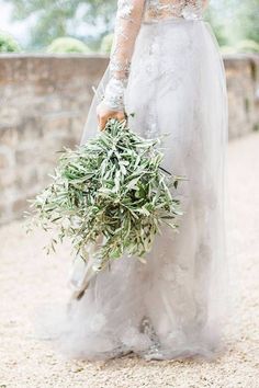 a bride holding a bouquet of greenery in her hand