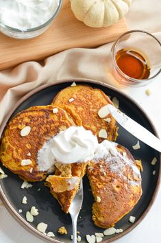 two pancakes on a plate with whipped cream and pumpkins in the background, one being eaten by a fork