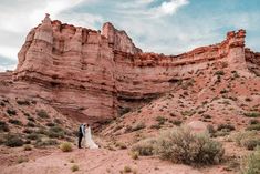 a bride and groom standing in front of red rock formations at the base of a mountain