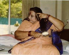 a woman sitting on a bed brushing her hair