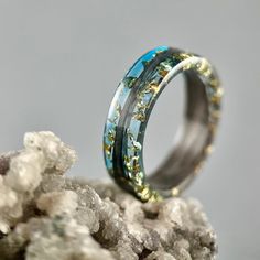 a wedding ring with blue and yellow flowers on it sitting on top of some rocks