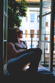 a woman is sitting on a balcony talking on her cell phone and looking out the window