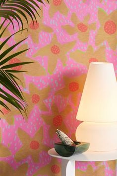 a lamp sitting on top of a white table next to a wall with pink and green designs