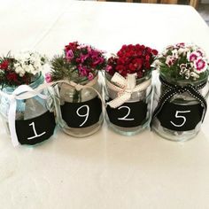 four jars with flowers in them are labeled number twenty five and decorated with ribbons on the table