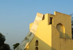 a yellow building with an arched window on the side and a bird flying in the background