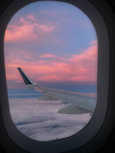 an airplane window with the view of clouds and sky at sunset from inside one plane