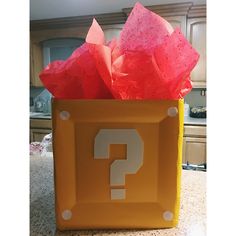 a yellow box with red tissue paper in it and a question mark on the front