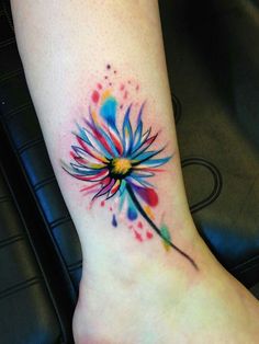 a watercolor tattoo on the ankle of a woman's foot with a colorful dandelion