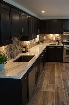 a kitchen with black cabinets and marble counter tops, stainless steel appliances and wood flooring