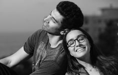 a man and woman sitting next to each other near the ocean in black and white