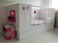 a white crib with pink accents in a child's room, next to a bed and dresser