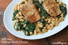 two pieces of fish on top of beans and spinach in a white bowl with a wooden table