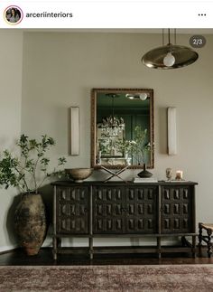 a room with a mirror, vases and plants on the table in front of it