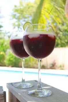 two glasses of wine sitting on top of a wooden table next to a swimming pool