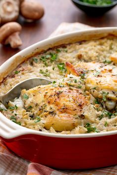 a red casserole dish filled with chicken and rice, garnished with parsley