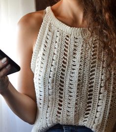 a woman holding a cell phone in her right hand and wearing a crochet top