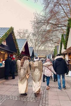 two women walking down the street in front of christmas decorations and trees with lights on them