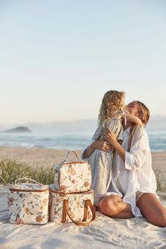 two women are sitting on the beach with their suitcases and one woman is kissing her