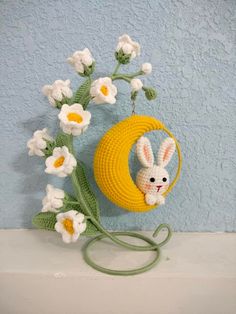 a crocheted bunny in a basket with daisies on the side next to a blue wall