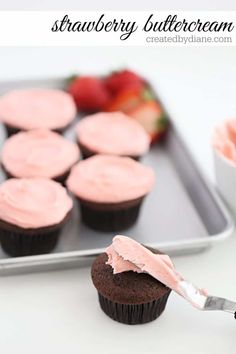 strawberry frosting on top of cupcakes in front of a tray with strawberries