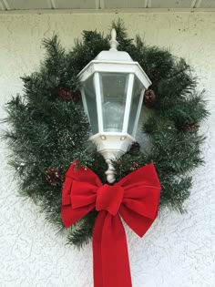 a wreath with a red bow hanging on the side of a white wall next to a light