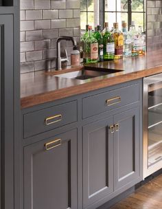 a kitchen with grey cabinets and wooden counter tops, along with wine bottles on the shelves