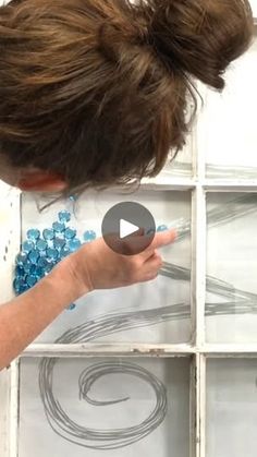 a woman is painting on the wall with white paint and some blue beads in front of her