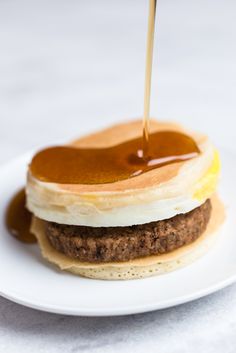 pancakes with syrup being poured onto them on a white plate