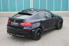 the back end of a black bmw car parked in front of a blue garage door