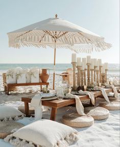 an umbrella is set up on the beach for a dinner party with white linens and candles