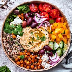 a bowl filled with vegetables, chickpeas and hummush sauce on top